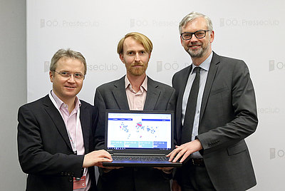 Von links: Dr. Christoph Steindl, CEO Catalysts, Patrick Haebig, Brand Manager Catalysts, und Wirtschafts-Landesrat Dr. Michael Strugl von vorne fotografiert. Mittlere Person hält Laptop in der Hand. Der Bildschirm zeigt in Richtung Kamera.